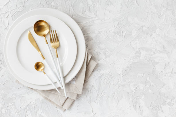 Beautiful gold and white cutlery on white plate on light white gray background stock photo