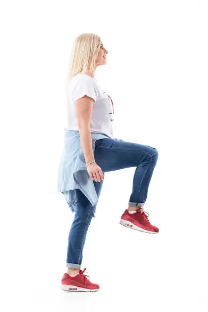 Success concept. Happy middle age casual woman walking up climbing on invisible stairs looking up. Full body length isolated on white background.