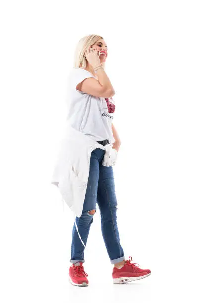 Side view of happy cheerful mid age woman in casual clothes walking and talking on cellphone. Full body length isolated on white background.