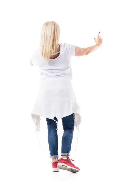 Back view of blonde mid age woman pointing finger pushing button on interactive virtual screen. Full body length isolated on white background.