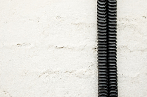 Electric wires in a protective corrugated hose attached to an old white wall