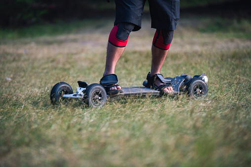 Unrecognizable man riding electric off road skateboard in nature.