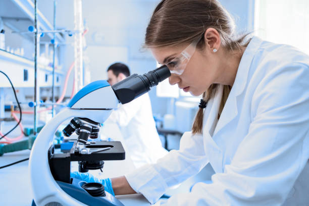 istock Female Scientist Working in laboratory looking through microscope wearing protective glasses 1217229134