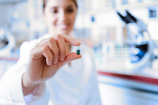 medizinarzt hält eine farbkapsel pille in der hand mit weißen handschuh im labor - pharmacy pharmacist smiling pill stock-fotos und bilder