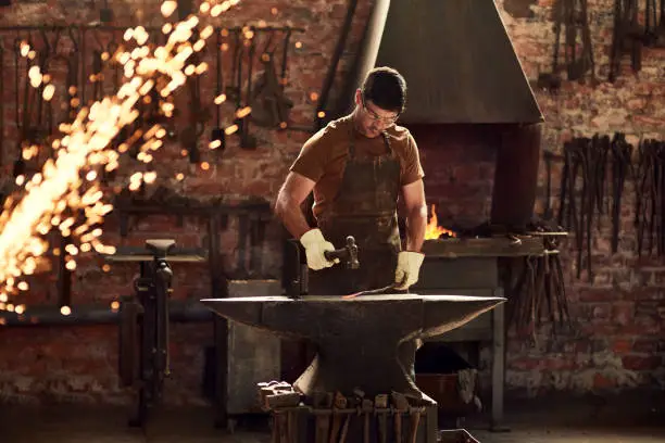 Cropped shot of a handsome young metal worker hitting a hot metal rod with a sledgehammer in a welding workshop