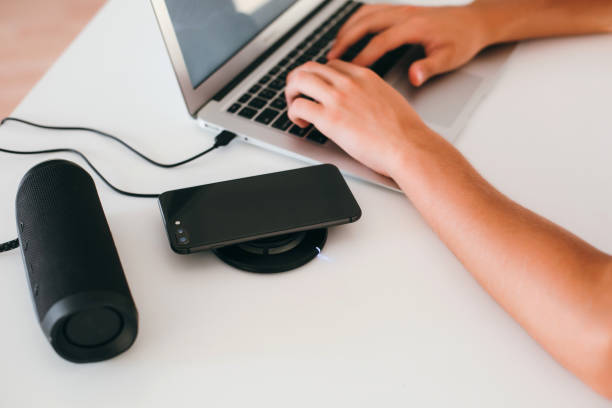 Man's hands working on laptop, wireless speaker and wireless phone charger