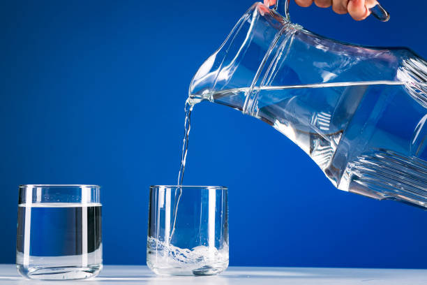 istock Hand pours water from jug into a glass isolated blue background 1217235353
