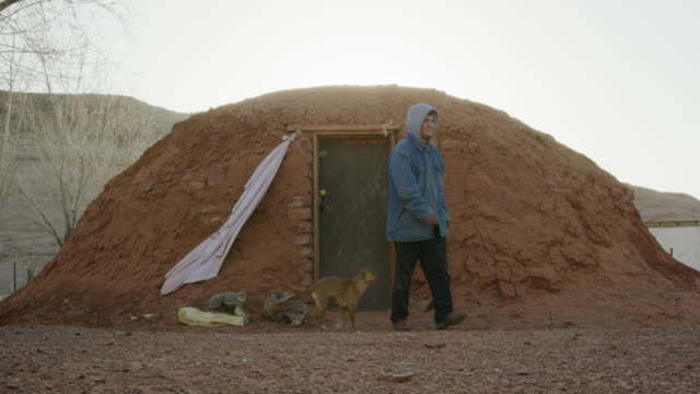 A Native American (Navajo) Teenaged Boy Opens the Door and Exits a Mud Hogan (Navajo Hut) and Is Met by His Pet Dog