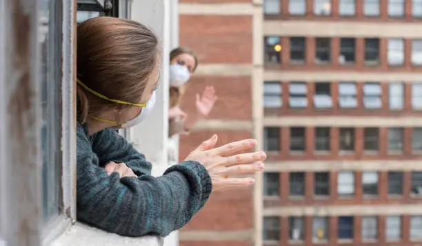 Two downtown apartment neighbors waving to each other during shelter-in-place orders due to the Coronavirus pandemic of 2020.