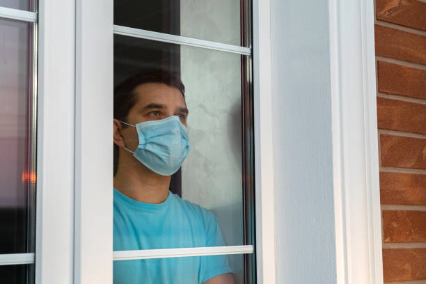 istock Young man in medical mask is looking out window 1217241335