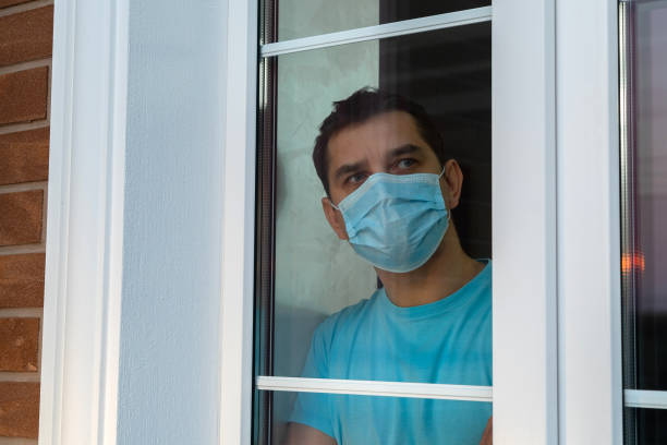 istock Young man in medical mask is looking out window 1217241352