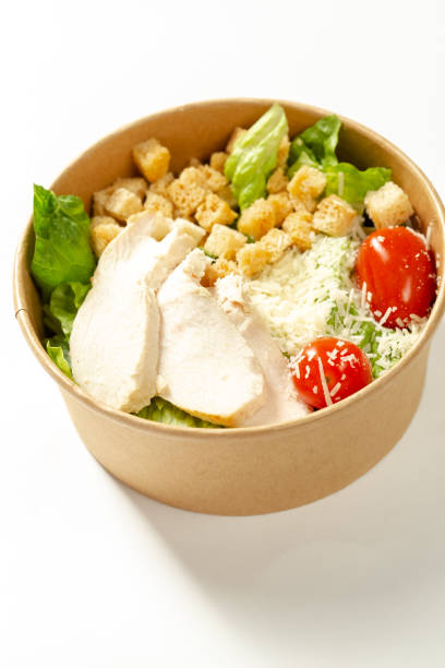 istock White isolated background, in a cardboard plate or package, Caesar salad with chicken, lettuce, cherry tomatoes 1217245085