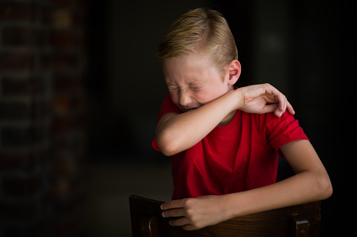 A young 11-year old blond Caucasian boy demonstrating the correct way to cough and sneeze into an elbow rather than using hands to stop the spreading of the Coronavirus during lockdown in South Africa due to the COVID-19.