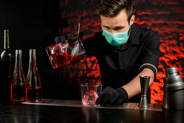istock Professional bartender with mask pours cold cocktail into glass. 1217250821