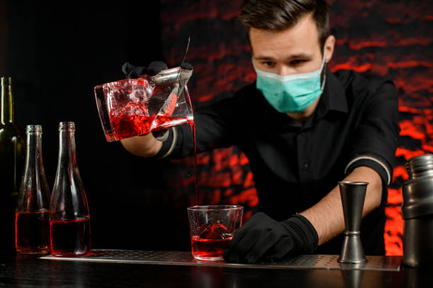 istock Barman with mask masterfully pours cold cocktail into glass. 1217251074