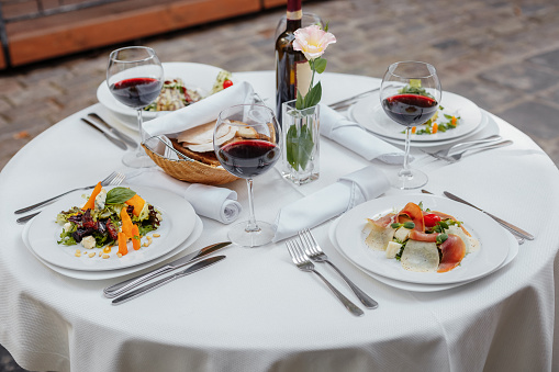 Served table for four with a bottle of wine, salads, glasses on the street waiting for guests