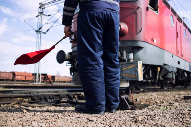 Railroad worker or switchman with red flag standing by the rail tracks as train passing by at the station. Railroad worker or switchman with red flag standing by the rail tracks as train passing by at the station. railway signal stock pictures, royalty-free photos & images