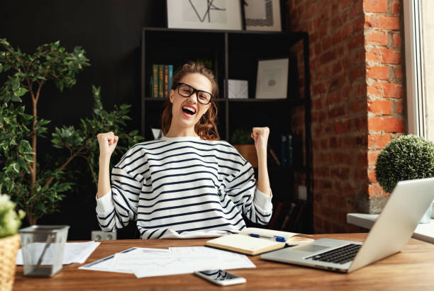 istock Excited woman celebrating victory while working at laptop in loft office 1217255372
