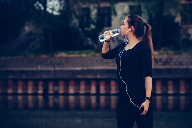 istock Female runner standing by the river and drinking water from a bottle 1217261234