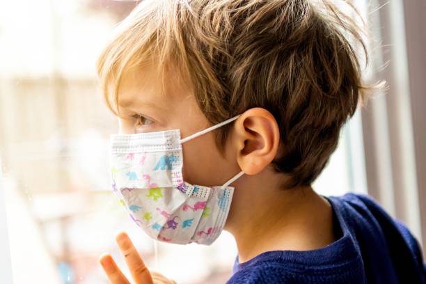 istock Little child boy looking through a window using a surgical mask 1217265052