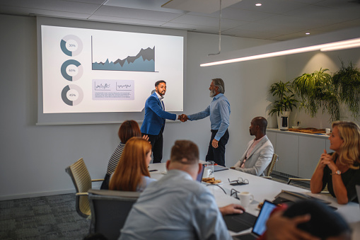 African businessman shaking hands with mature bearded executive and introducing him as next speaker at seminar.