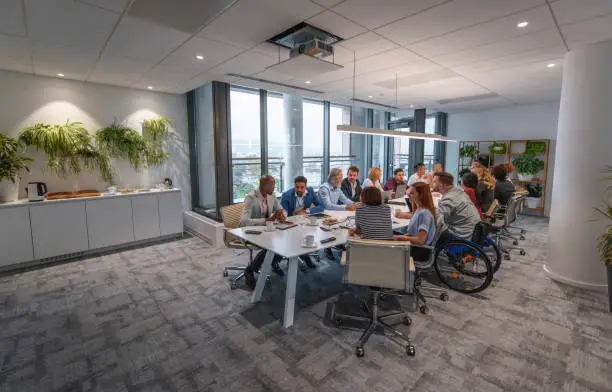 Distant view of diverse group of business people sitting at conference table in office board room waiting for meeting to begin.