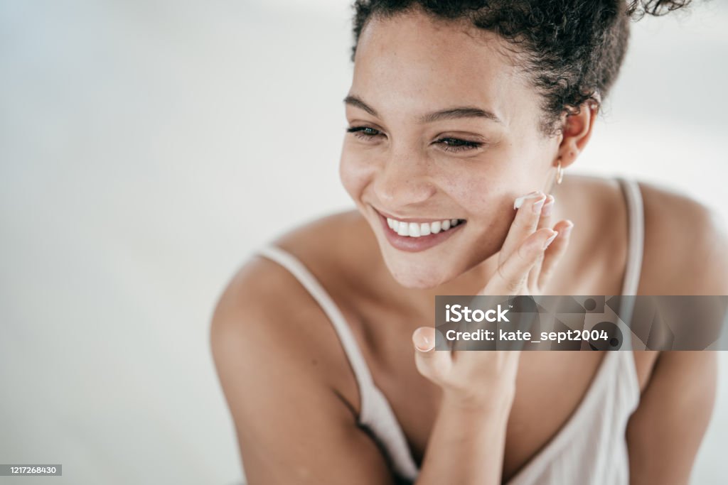 Smiling young women applying moisturiser to her face Skin Care Stock Photo