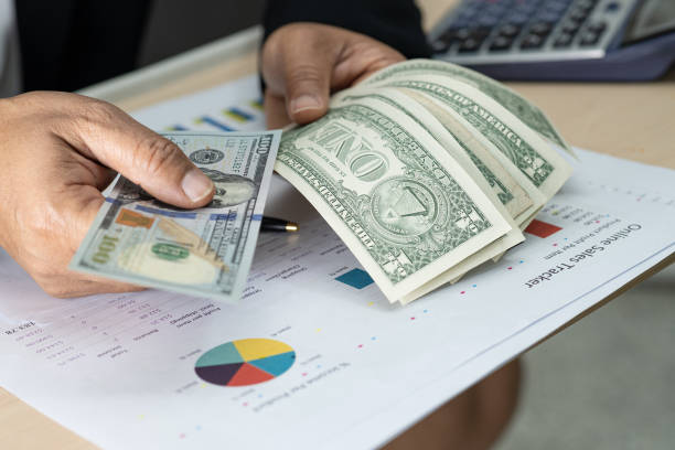 istock Asian accountant holding dollar banknotes, working, calculate and analyzing report project accounting with calculator and graph report in modern office : finance and business concept. 1217270996