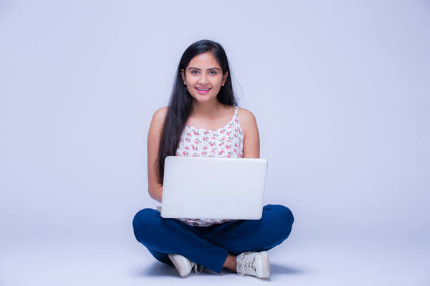 Young Girl With Laptop at white background - stock images Indian Ethnicity, Lifestyle, Student, Teenage Girl, Modern, White Background, cross legged photos stock pictures, royalty-free photos & images