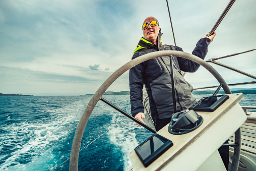 Caucasian businessman in casual clothing talking on mobile phone for corporate business while travel on luxury catamaran boat yacht sailing in the ocean on summer holiday vacation.