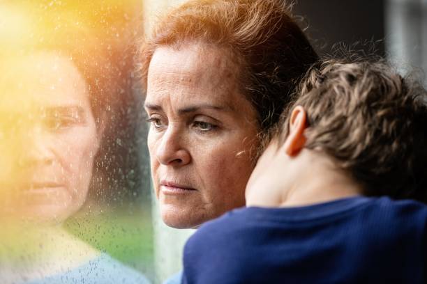 mature woman posing with her son, very sad looking through window worried about covid-19 lockdown - unemployment fear depression women imagens e fotografias de stock