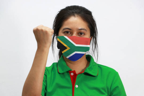 South Africa flag on hygienic mask. Masked woman prevent germs and wear green shirt. Tiny Particle or virus corona or Covid-19 protection. Lift the fist up for meaning fighting. stock photo