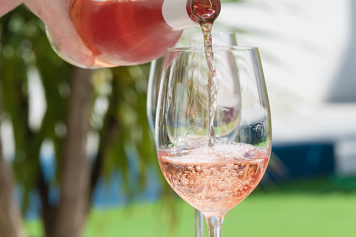 close up of a hand pouring delicious rose wine from bottle into glass outdoors . lifestyle concept