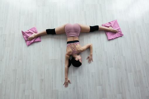 Young fitness woman does stretching exercise lying on the floor with her feet on mats.