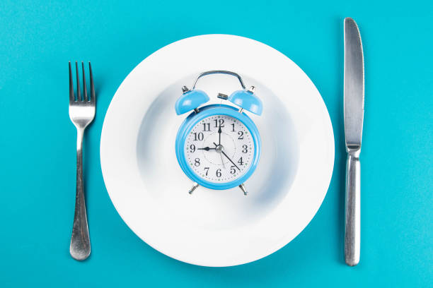 istock Alarm clock with fork and knife on the white plate on blue table. Time to eat, Breakfast, Lunch Time and Dinner concept 1217287782