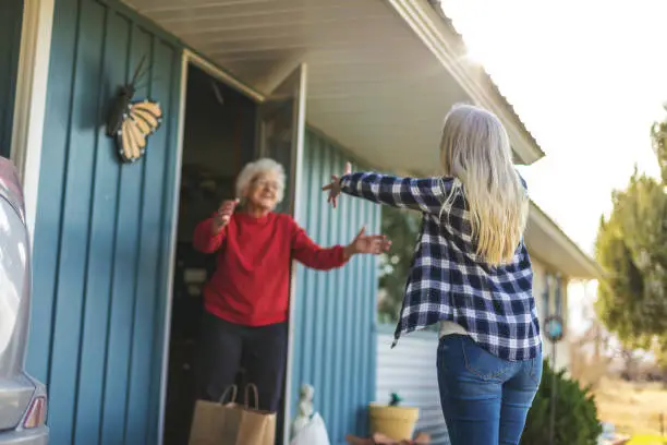 Photo of Mature Adult Female Delivering Groceries to Senior Adult Female and Social Distancing Due to Infectious Virus Outbreak Pandemic