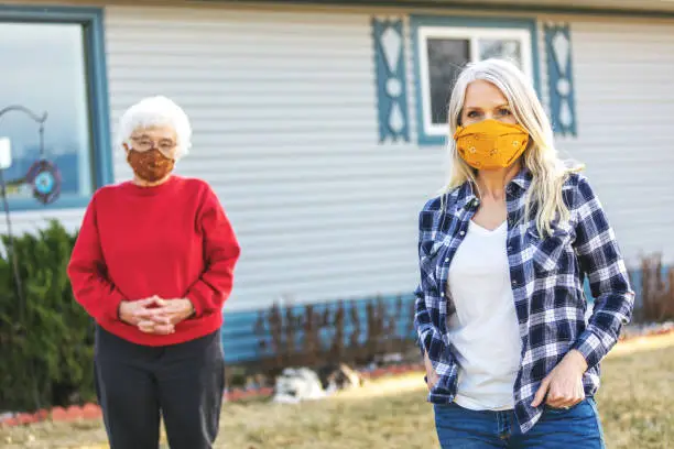 Photo of Mature Adult Female and Senior Adult Female Wearing Face Masks and Demonstrating Social Distancing Due to Infectious Virus Outbreak Pandemic