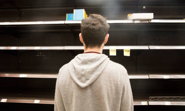 Man shopping in supermarket out-of-stock, looking at empty shelves. Young man standing looking at empty shelves in supermarket.  Empty shelves due to panic buying. sold out photos stock pictures, royalty-free photos & images
