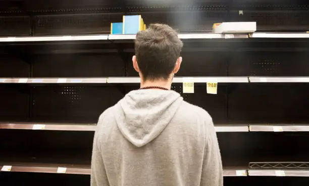 Young man standing looking at empty shelves in supermarket.  Empty shelves due to panic buying.