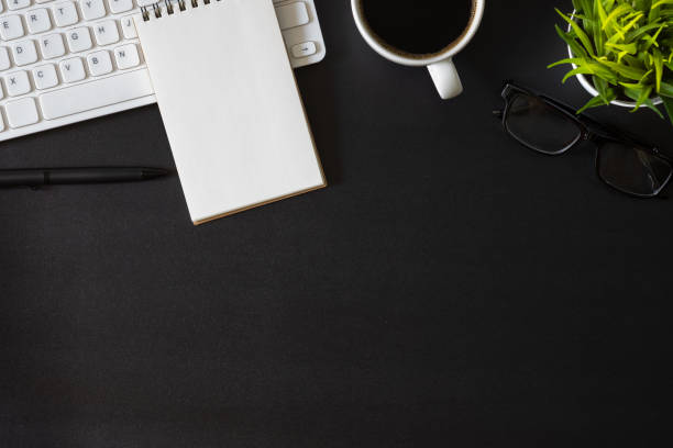 istock Workplace office with dark black desk. Top view from above of keyboard with notepad and coffee cup. Space for modern creative work of designer. Flat lay with copy space. Business and  finance concept. 1217297727
