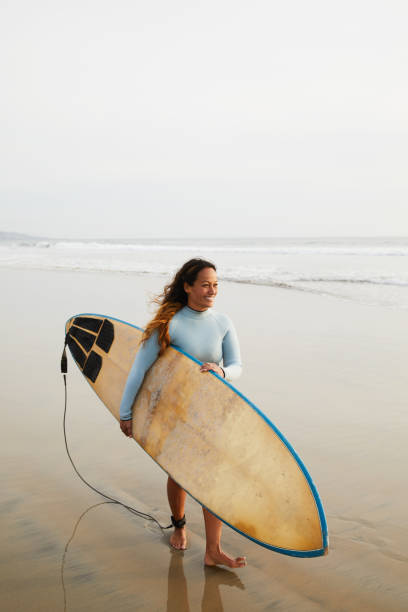 istock Smiling mature woman walking on a beach with her surfboard 1217299882