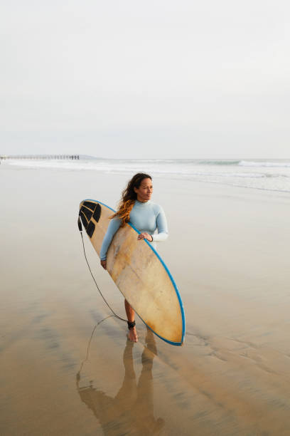 istock Mature woman walking alone on a beach with her surfboard 1217299919