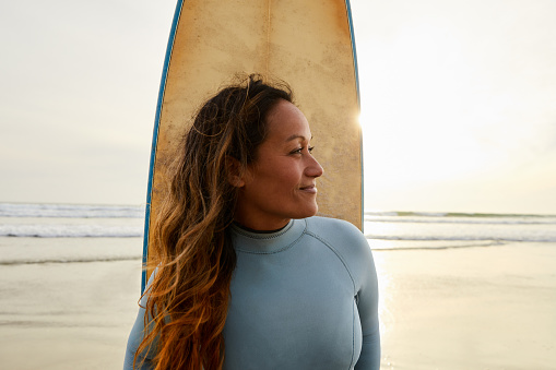 Smiling mature woman standing on a beach with her surfboard