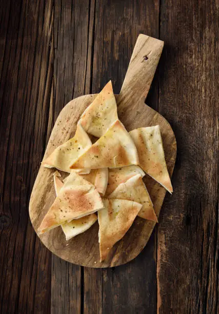 Crispy homemade pita bread chips with seasoning on a wooden cutting board
