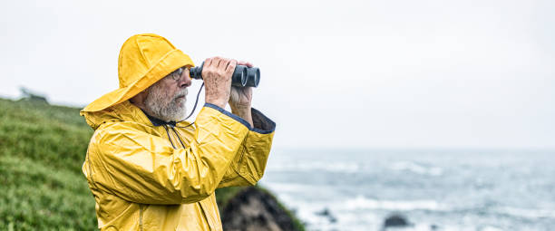 istock Sea Mariner Man in Yellow Raincoat Looking Through Binoculars 1217303176