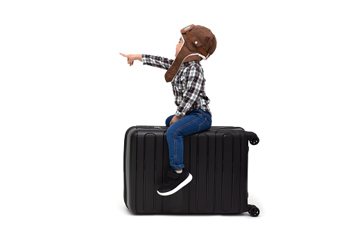 Happy kid Asian boy sitting on a black suitcase and pointing finger to copy space isolated over white background, Dreams of travel concept, Two year one month old