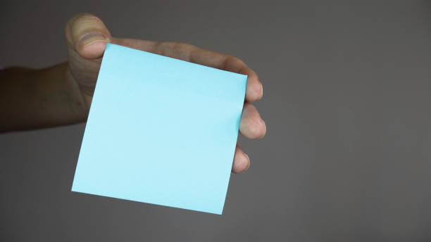 istock Hand holding a blank sticker. Square paper with space for text in the hand. Sticky note with in a hand 1217325156