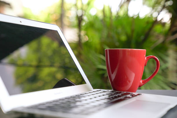 Red coffee cup with computer laptop. Green nature background.