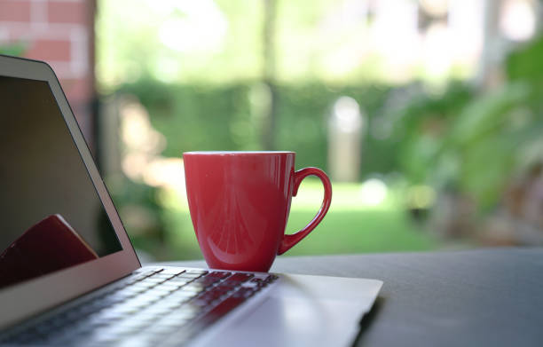 istock Red coffee cup with computer laptop. Green nature background. 1217326307