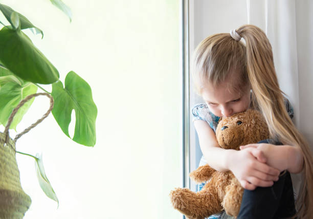 istock Sad child girl by the window 1217326812